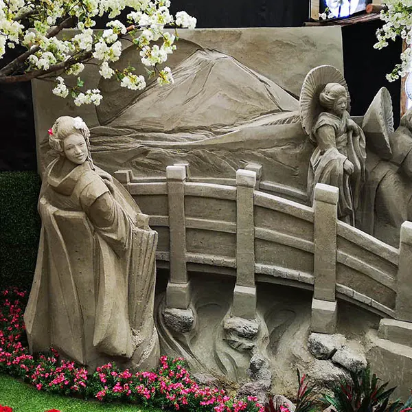 Escultura de arena de un jardín japonés, con un puente, figuras y el monte Fuji al fondo.