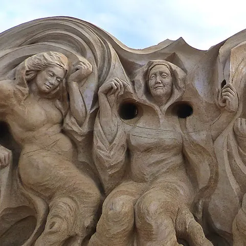 Escultura de arena con figuras de las nornas entre pliegues de tela.